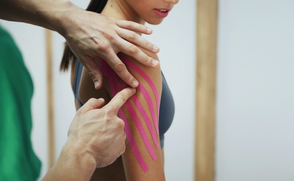 Doctor helps woman by shoulder treatment with kinesio tape